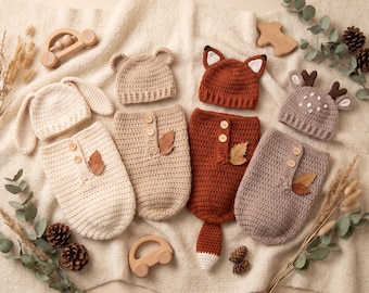 May include: Four sets of crocheted baby cocoons and matching hats in animal themes including a cream bunny, a tan bear, a rust-colored fox with a tail, and a mauve deer with antlers. Each cocoon features two wooden buttons and a small dried leaf.