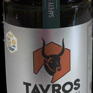 May include: A silver jar of Tavros Hellenic Bio Honey, labeled "Wild Forest" and "Limited Production". The jar features a green safety seal and a logo of a black bull's head inside a hexagon.