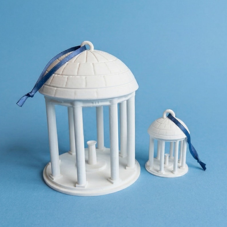 UNC Chapel Hill Old Well ornaments, shown side by side, in a Carolina Blue background.