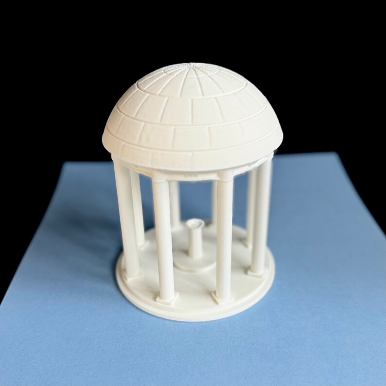 The UNC Old Well figurine, shown against a Carolina Blue background.