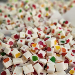 May include: A close-up of a pile of white candy cubes with colourful sprinkles. The candy is arranged in a random pattern, with some cubes stacked on top of others.