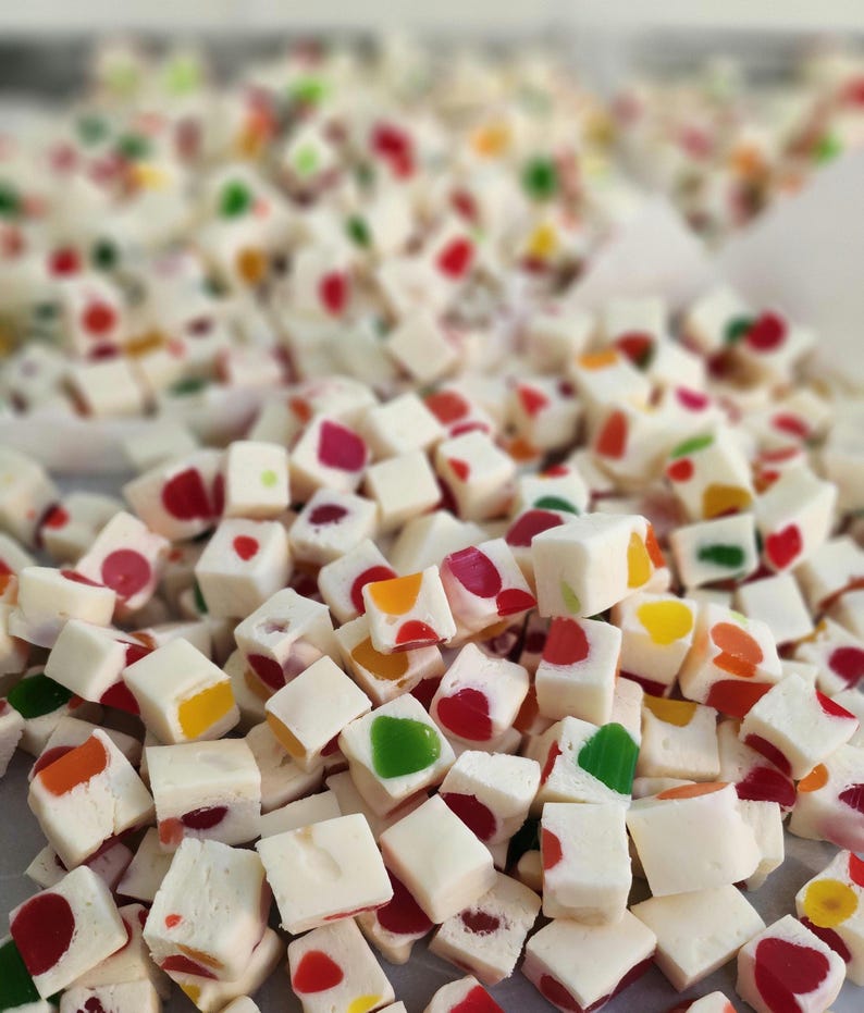 May include: A close-up of a pile of white candy cubes with colourful sprinkles. The candy is arranged in a random pattern, with some cubes stacked on top of others.