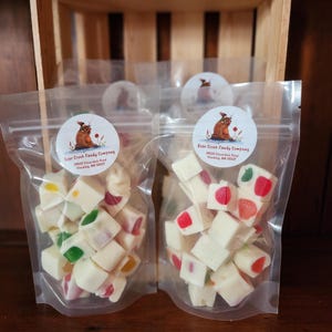 May include: Two clear plastic bags filled with white fudge cubes with colourful candies inside. The bags are labelled "Bear Creek Candy Company" with an address and phone number.