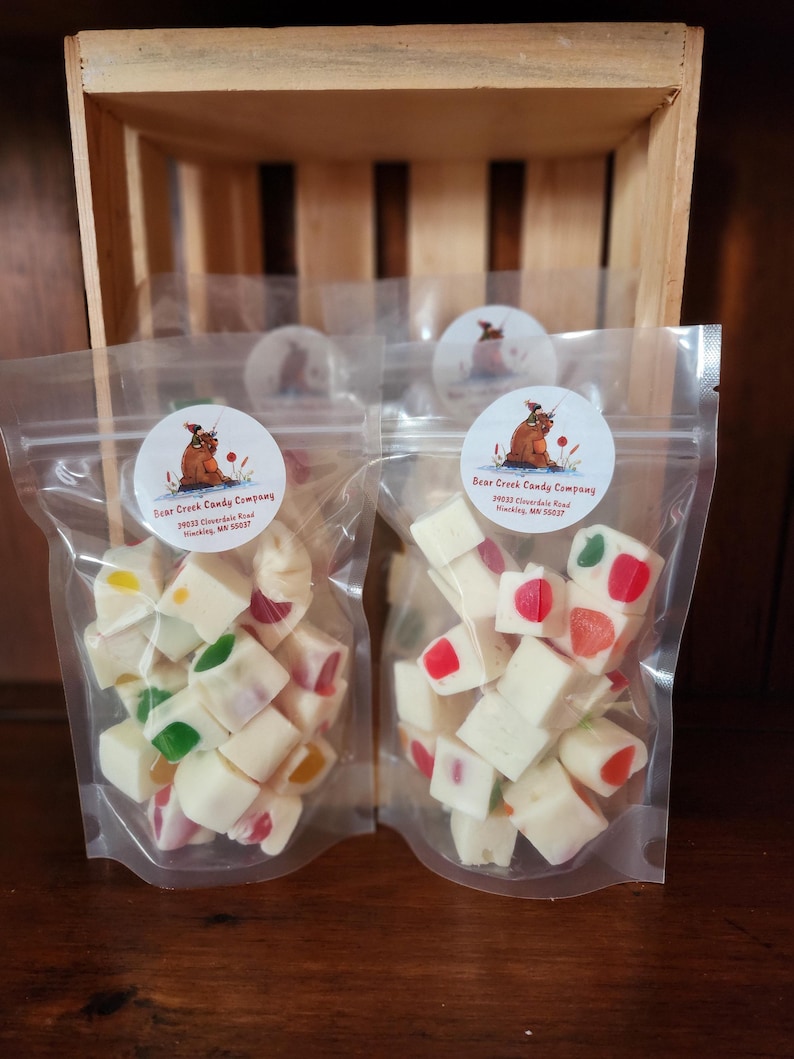 May include: Two clear plastic bags filled with white fudge cubes with colourful candies inside. The bags are labelled "Bear Creek Candy Company" with an address and phone number.
