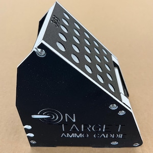 May include: Black metal ammo caddie with a perforated top and white accents. The caddie has the text "ON TARGET AMMO CADDIE" and the number "308" etched into the metal. The caddie is designed to hold ammunition.