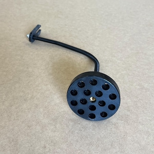 May include: A black, flexible gooseneck camera mount with a circular base. The base has multiple holes and a threaded brass insert. The mount has a small clamp at the end.