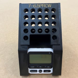 May include: A black plastic stand with a grid of holes and the text "7-6.5PRCW" on the top. A white digital timer with a black face is sitting in the stand. The timer has buttons labeled "Hour", "Min", "Sec", "Start/Stop", "Clear", and "Mode".