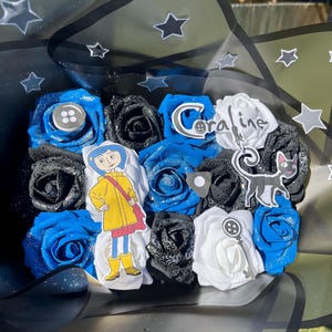 May include: A bouquet of artificial roses in blue, black, and white, with decorative accents. The bouquet includes a character cutout, a button, a key, and the word "Coraline". The bouquet is wrapped in black cellophane with star accents.