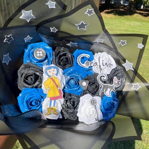 May include: A bouquet of blue, black, and white roses wrapped in black and green cellophane with star accents. The bouquet includes character cutouts and the word "Coraline".