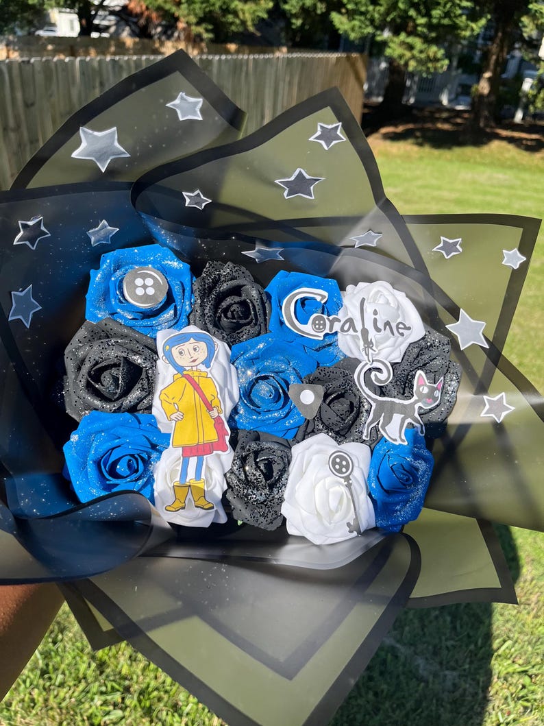 May include: A bouquet of blue, black, and white roses wrapped in black and green cellophane with star accents. The bouquet includes character cutouts and the word "Coraline".