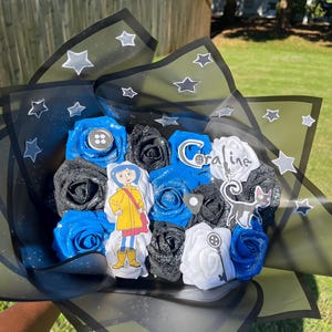 May include: A bouquet of blue, black, and white artificial roses, with a decorative wrapping featuring star patterns. The bouquet includes character cutouts and a button accent, creating a themed floral arrangement.