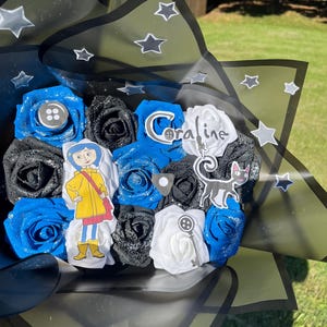 May include: A bouquet of artificial roses in blue, black, and white, with glitter accents. The bouquet includes character cutouts and the name "Coraline". The arrangement is wrapped in black and green paper with star accents.