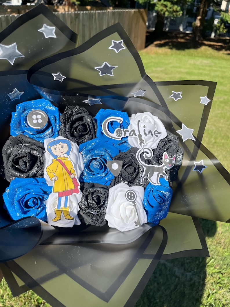 May include: A bouquet of artificial roses in blue, black, and white, with glitter accents. The bouquet includes character cutouts and the name "Coraline". The arrangement is wrapped in black and green paper with star accents.