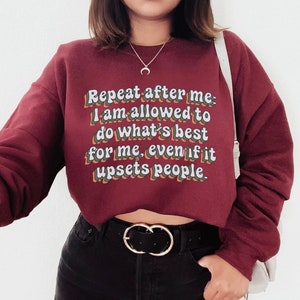 May include: A maroon cropped sweatshirt with the text "Repeat after me: I am allowed to do what's best for me, even if it upsets people." in a retro font.