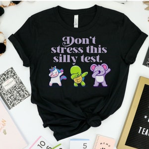 May include: Black t-shirt with the text "Don't stress this silly test." in purple. The shirt features a unicorn, turtle, and koala doing the "dab" dance.
