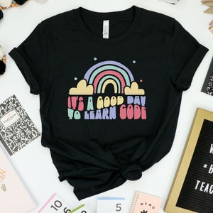 Puede incluir: Camiseta negra con un arcoíris y el texto "It's a good day to learn code" en letras de colores.