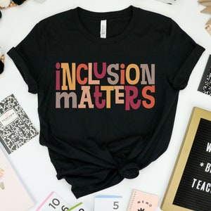 Puede incluir: Camiseta negra con el texto "inclusion matters" en letras de bloque de colores. Las letras son en tonos de rojo, naranja, amarillo y marr&oacute;n.