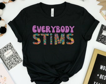 Könnte beinhalten: Schwarzes T-Shirt mit dem Text "EVERYBODY STIMS" in lila und bunten Blumenbuchstaben.