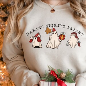 May include: A cream-coloured sweatshirt with the text "Making Spirits Bright" and three ghosts wearing Santa hats. The ghosts are holding a star, a gift box, and a stocking.