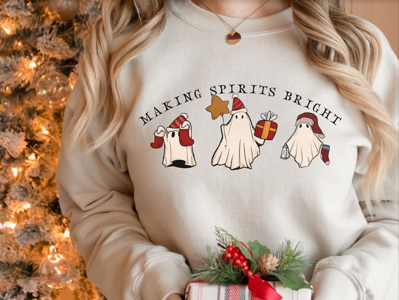 May include: A cream-coloured sweatshirt with the text "Making Spirits Bright" and three ghosts wearing Santa hats. The ghosts are holding a star, a gift box, and a stocking.