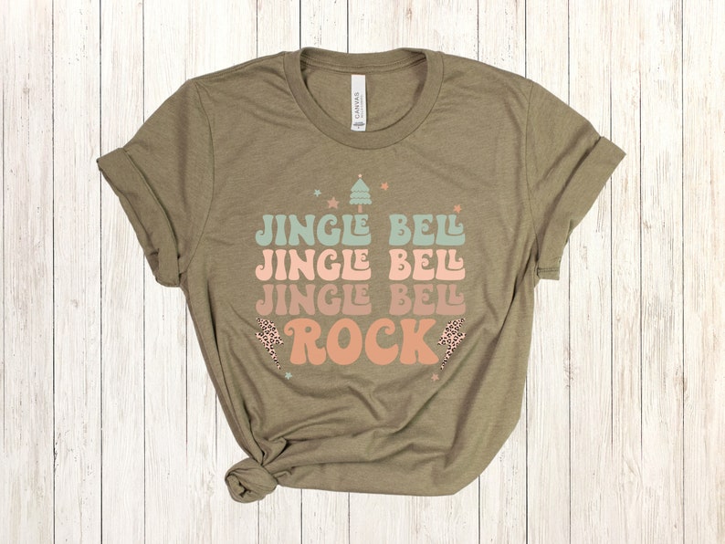 May include: A green t-shirt with the text "Jingle Bell Jingle Bell Jingle Bell Rock" in a retro font. The text is in shades of pink, blue, and green. There are small stars and a lightning bolt with a leopard print design.