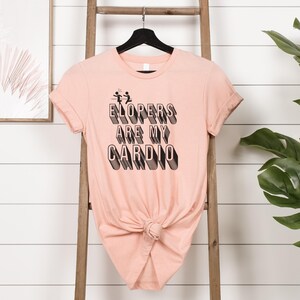 May include: A peach-colored t-shirt with a black graphic that reads "Elopers are my cardio" with a stick figure couple running away.