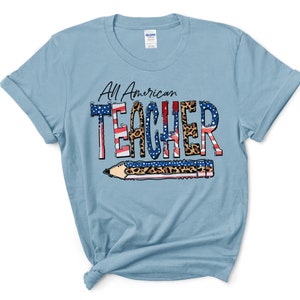 May include: Light blue t-shirt with the text "All American Teacher" in black lettering with a red, white, and blue American flag design and leopard print accents. The text is surrounded by a pencil with a leopard print design.