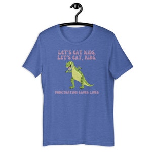 May include: A blue t-shirt featuring a green dinosaur graphic and the text "Let's eat kids. Let's eat, kids. Punctuation saves lives."