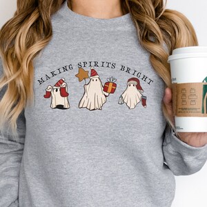 May include: Grey sweatshirt with the text "Making Spirits Bright" and a graphic of three ghosts wearing Santa hats. One ghost is holding a star, another is holding a gift, and the third is holding a cup of coffee.