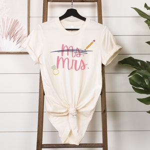May include: A white t-shirt with the text "Mrs." written in pink with a line through "Ms." and a pencil drawn above the line. A diamond ring is drawn to the left of the text.