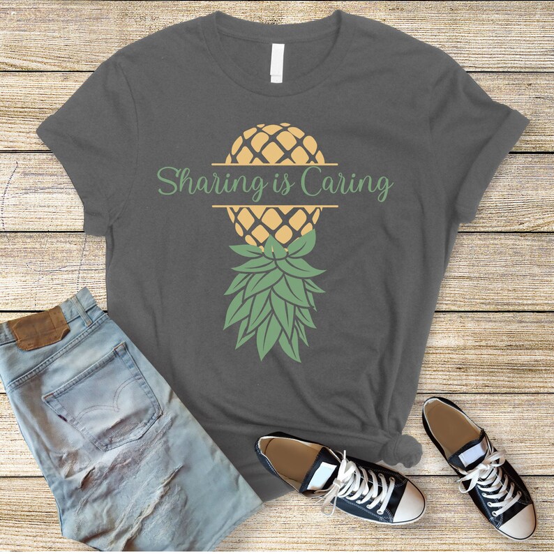 Puede incluir: Una camiseta gris oscuro con un gr&aacute;fico de pi&ntilde;a y el texto "Sharing is Caring" impreso en la parte delantera.