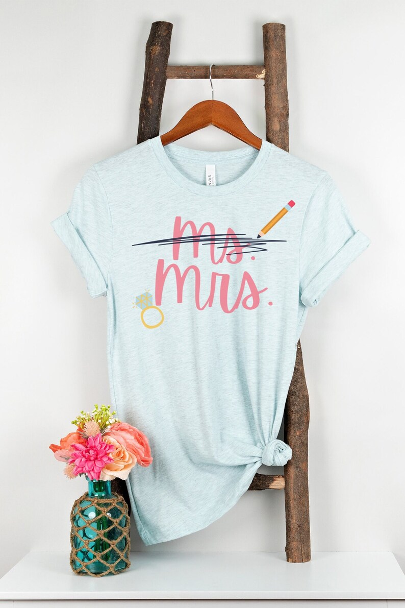 May include: A light blue t-shirt with the text "ms. mrs." in pink lettering. The word "ms." is crossed out with a black line and a pencil is drawn above the line. A diamond ring is drawn below the text.