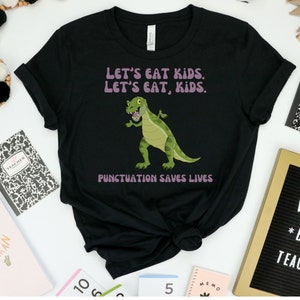 May include: Black t-shirt featuring a green dinosaur graphic and the text "LET'S EAT KIDS. LET'S EAT, KIDS. PUNCTUATION SAVES LIVES."