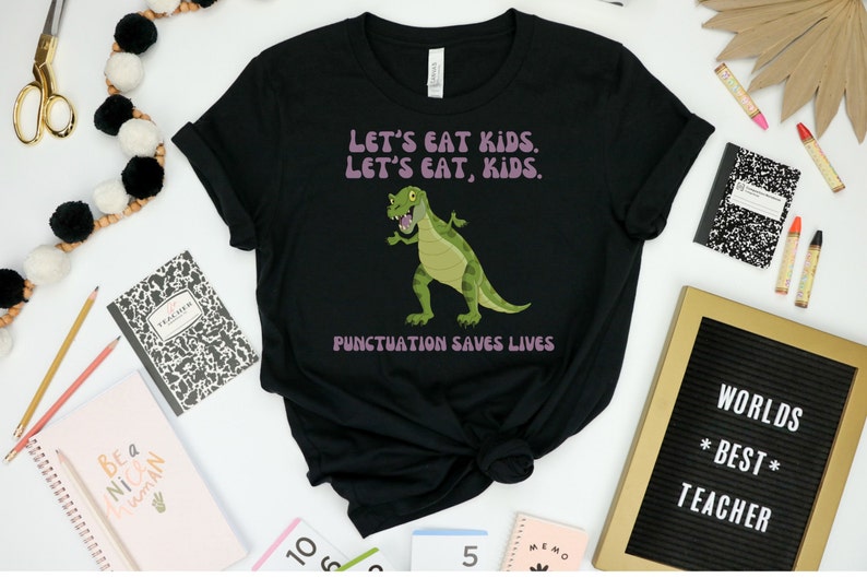 May include: Black t-shirt featuring a green dinosaur graphic and the text "LET'S EAT KIDS. LET'S EAT, KIDS. PUNCTUATION SAVES LIVES."