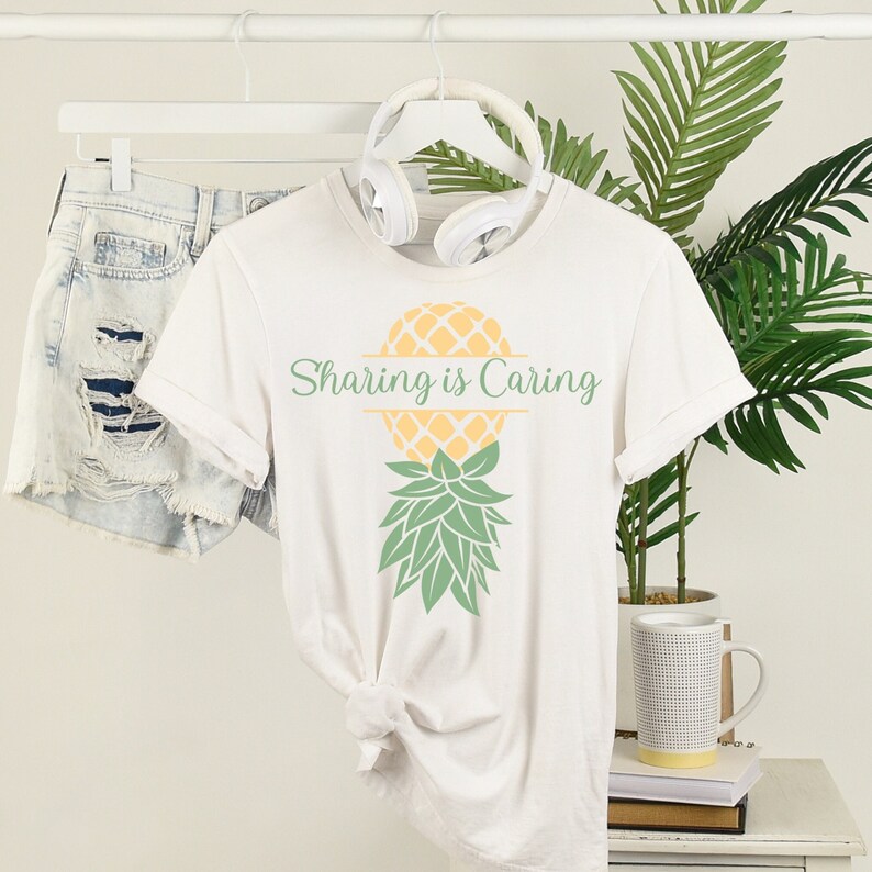 Puede incluir: Camiseta blanca con un gr&aacute;fico de pi&ntilde;a amarilla y el texto "Sharing is Caring" impreso en la parte delantera.