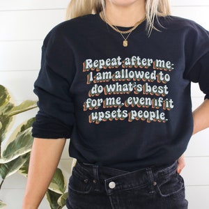May include: Black sweatshirt with a white graphic print that reads "Repeat after me: I am allowed to do what's best for me, even if it upsets people."