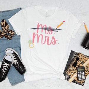 May include: White t-shirt with the text "Mrs." crossed out and "Mrs." written in pink below. A pencil is drawn above the crossed out text. A ring with a diamond is drawn to the left of the text.