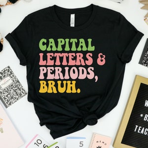 Puede incluir: Camiseta negra con un gr&aacute;fico de fuente retro colorido que dice "CAPITAL LETTERS & PERIODS, BRUH."