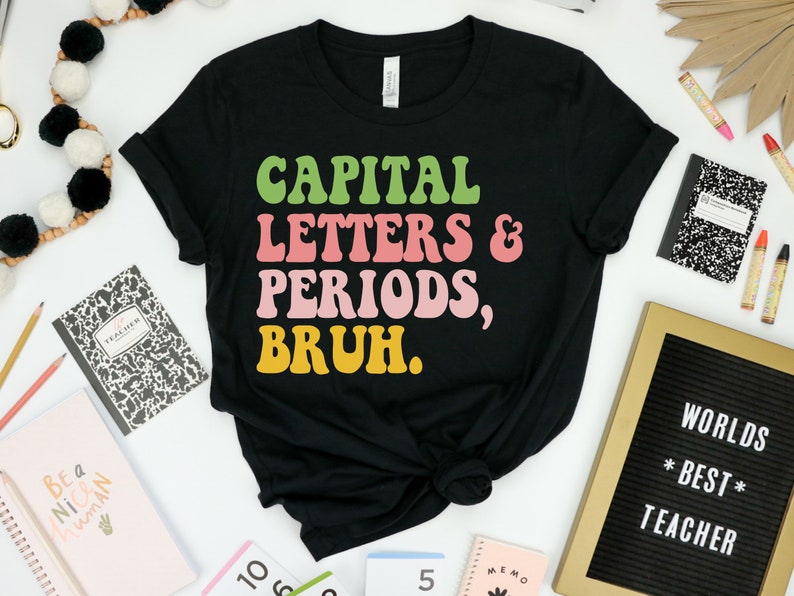 Puede incluir: Camiseta negra con un gr&aacute;fico de fuente retro colorido que dice "CAPITAL LETTERS & PERIODS, BRUH."