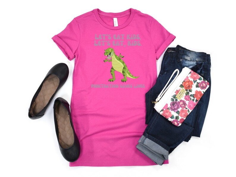 May include: Pink t-shirt featuring a green dinosaur graphic and the text "Let's eat kids, let's eat kids, punctuation saves lives".