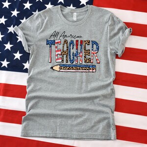 May include: Gray t-shirt with the text "All American Teacher" in red, white, and blue with a leopard print design. The text is layered over a pencil graphic.