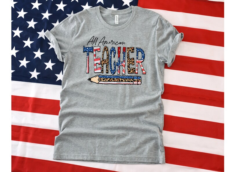 May include: Gray t-shirt with the text "All American Teacher" in red, white, and blue with a leopard print design. The text is layered over a pencil graphic.