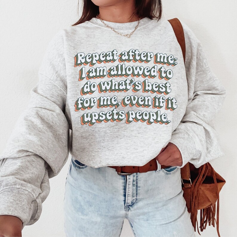 May include: A grey sweatshirt with the text "Repeat after me: I am allowed to do what's best for me, even if it upsets people." printed in a retro font with green, blue, and orange accents.