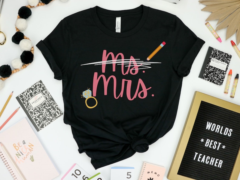 May include: Black t-shirt with the text "Ms. Mrs." in pink script with a diamond ring and a pencil drawn through the "Ms."