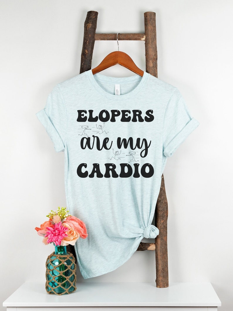 May include: Light blue t-shirt with the text "ELOPERS are my CARDIO" in black. The text is in a retro font style. There are stick figure drawings of people running around the text.