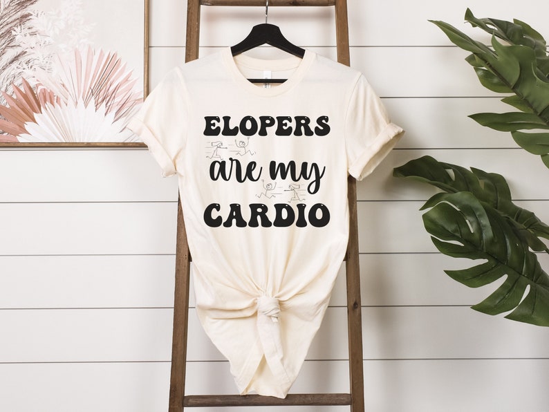 May include: A white t-shirt with black text that reads "Elopers are my cardio". The text is in a retro font style. There are stick figure drawings of people running around the text.