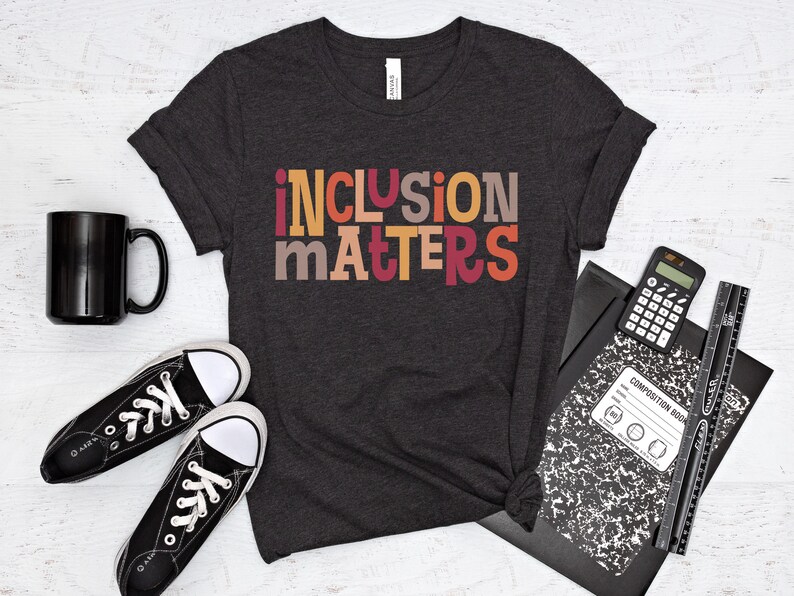 Puede incluir: Una camiseta gris oscuro con el texto "inclusion matters" en letras de bloque de colores. Las letras son en tonos de naranja, rojo, amarillo y marr&oacute;n.