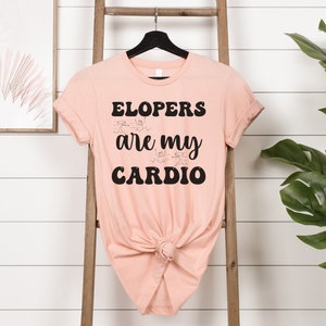 May include: A peach-colored t-shirt with black text that reads "ELOPERS are my CARDIO". The text is in a retro font style.