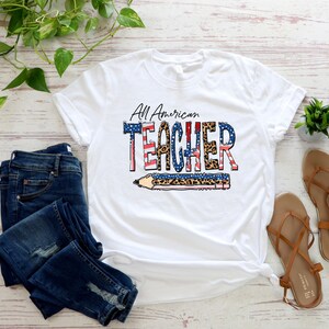 May include: White t-shirt with the text "All American Teacher" in red, white, and blue with a leopard print design. The text is over a pencil graphic with an American flag design.
