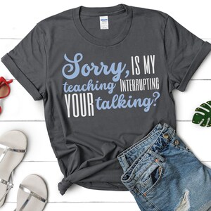 May include: A dark grey t-shirt with the text "Sorry, is my teaching interrupting your talking?" in white and blue lettering.